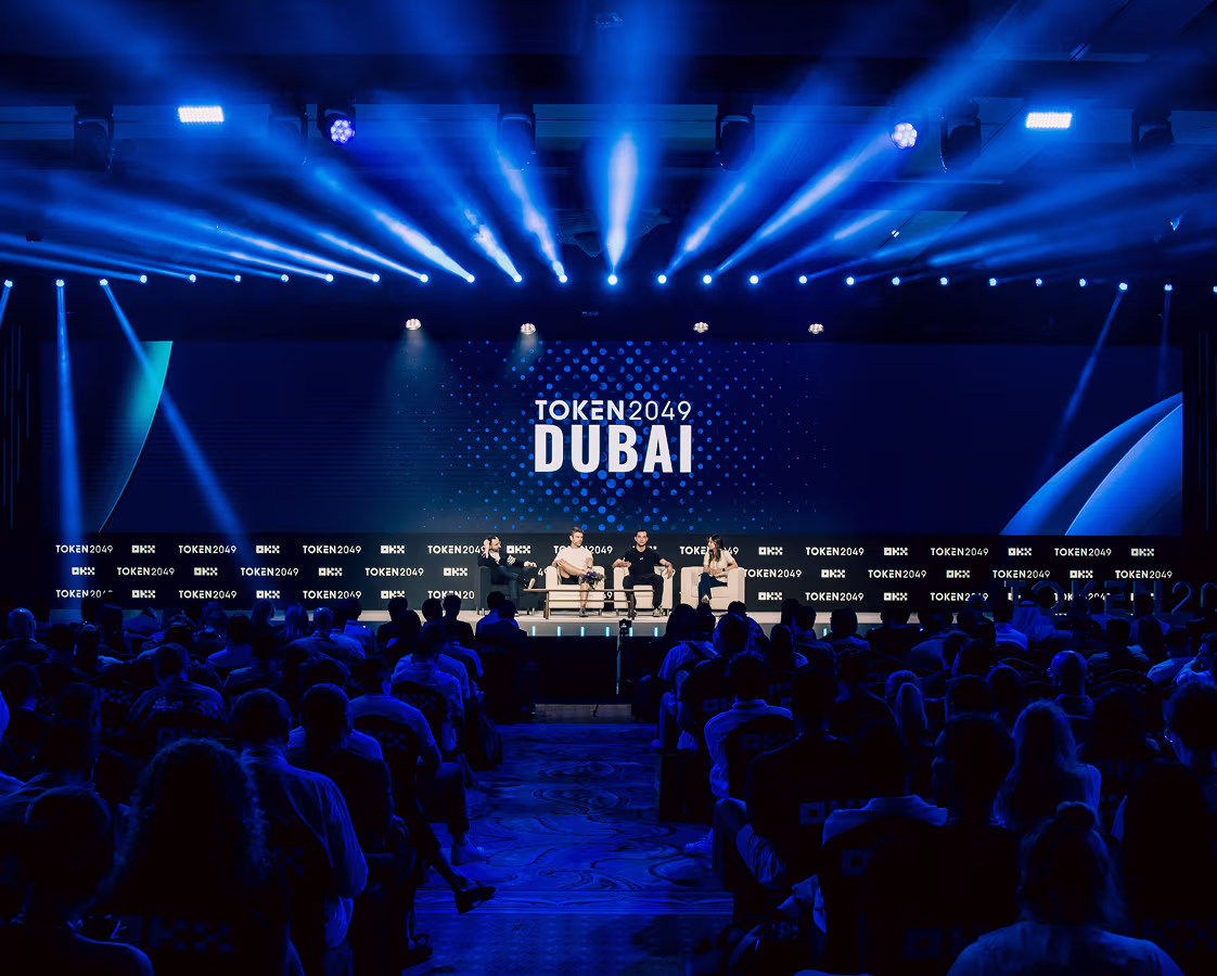 Panel discussion with four speakers on stage at TOKEN2049 Dubai conference under blue lighting.